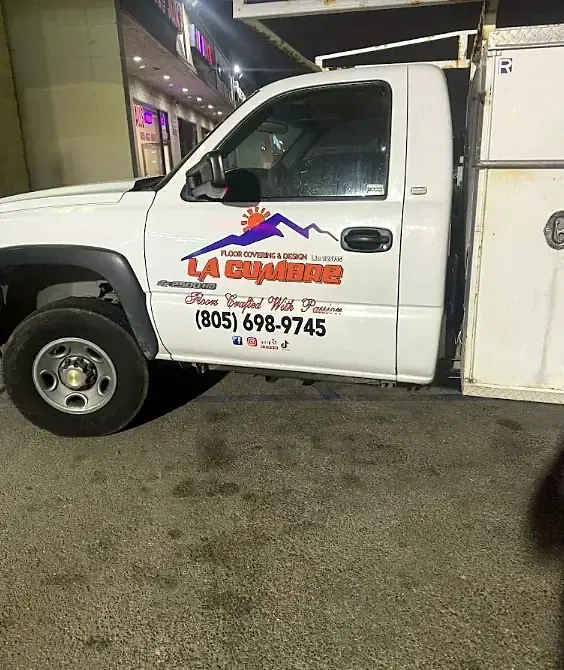 The door of a white work truck lettered La Cumbre Floor Covering and Design, Floors Crafted With Passion, with the phone number