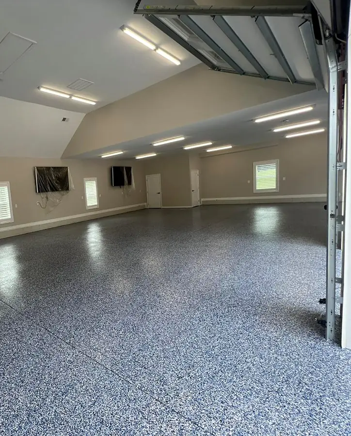 Large garage with a finished blue and gray flake epoxy floor, ceiling lights and a raised door
