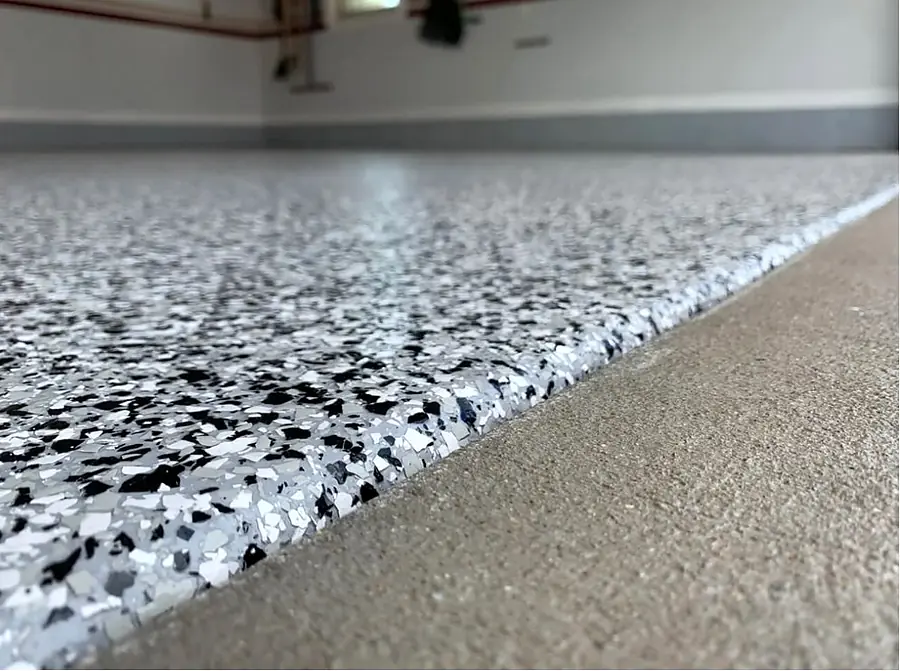 Close view of a flake epoxy floor edge, black, white and gray flakes meeting bare concrete