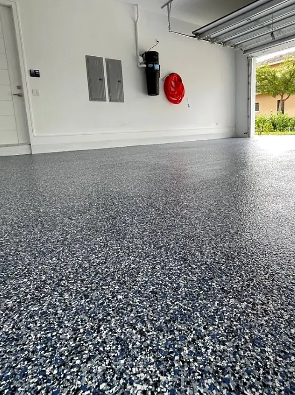 Finished flake epoxy floor in a garage with an open door, a fire extinguisher and an electrical panel on the wall
