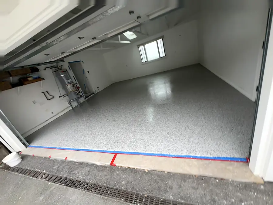 A garage floor with a gray flake coat in place, blue tape and red tape lines along the door threshold