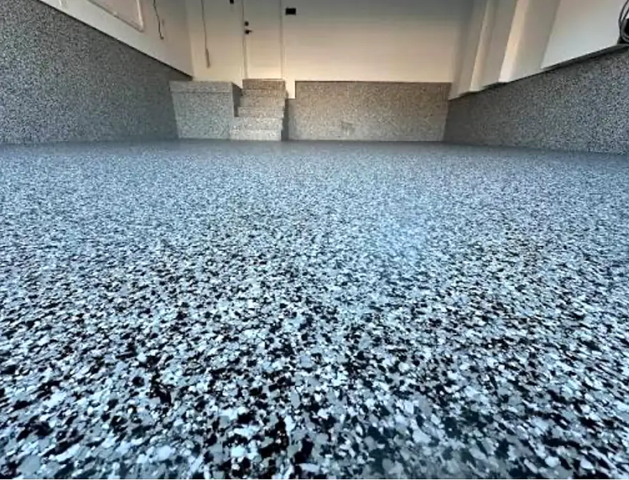 Wide view of a garage floor in gray, black and white flakes, with the same flake finish running up the base of the walls
