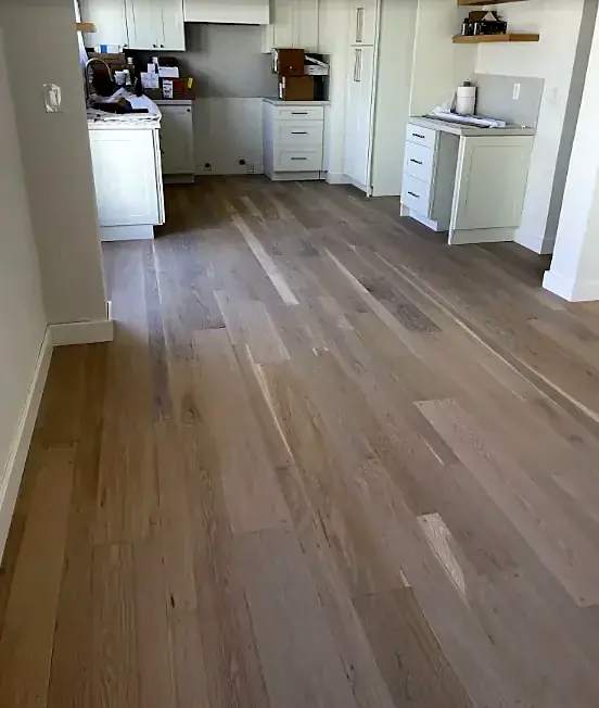 A white kitchen and hall with a floor of gray-toned wood planks