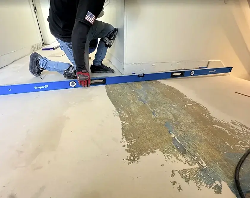 A crew member kneels and holds a six-foot level over a low spot marked on a slab
