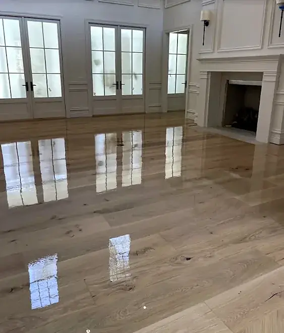A paneled room with a fireplace and a glossy wide plank floor mirroring three sets of French doors