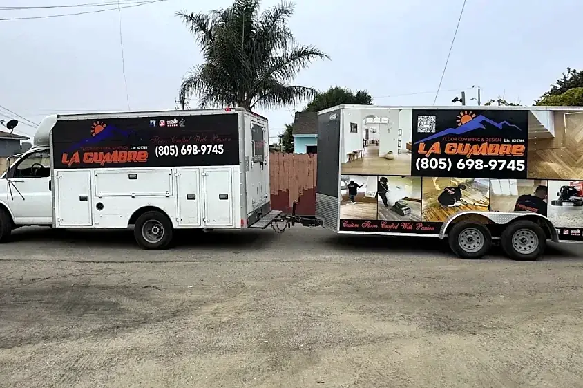 A white La Cumbre work truck towing an enclosed trailer wrapped with job photos and the phone number