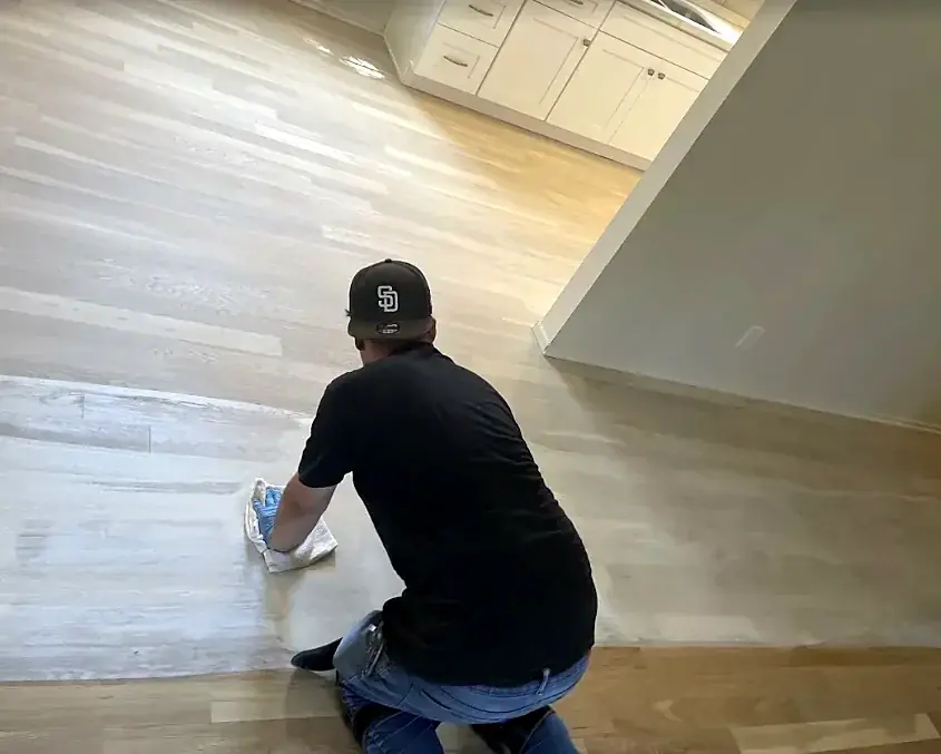 A crew member in a black cap kneels and wipes a floor with a rag, working toward the kitchen